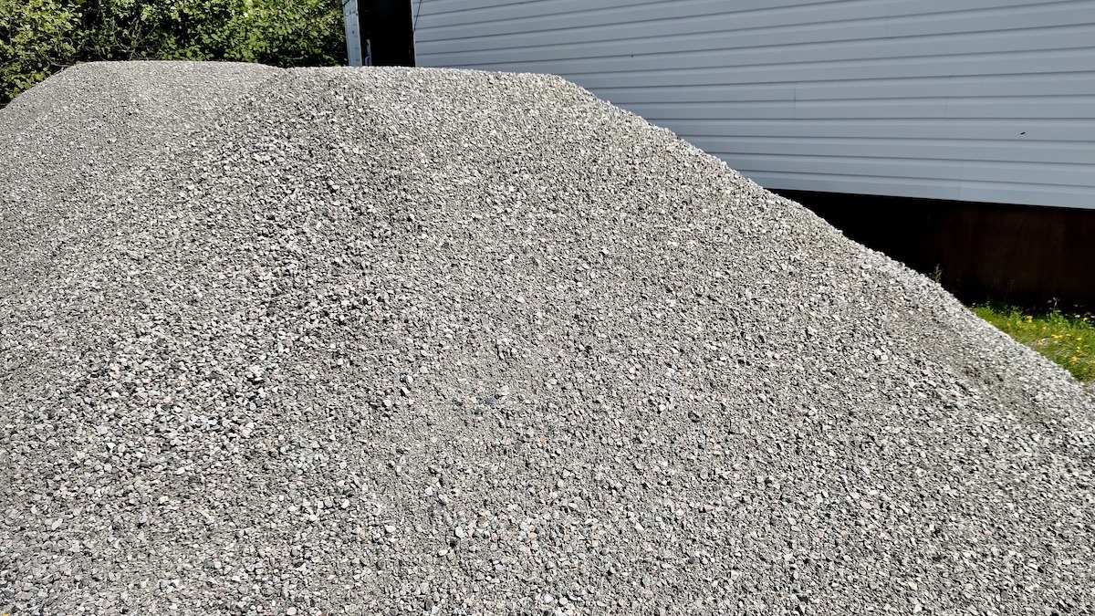 The first sign of progress! Piles of crushed gravel sit ready beside the Dyment Rec Hall, waiting to be laid down as sturdy concrete pads that will support accessible entrances and a new garden shed for the community garden.