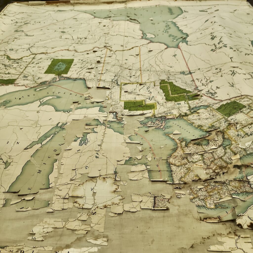 Rolled flat across several tables, the full scale of the massive multi-panel pull-down chart becomes clear. The Great Lakes basin and surrounding regions anchor the center, surrounded by decades of natural wear and paper separation along the canvas folds.